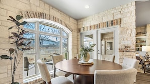 A dining room with a stone wall, a large window, and a round table with chairs.