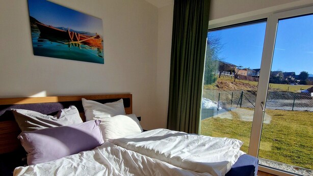 Een slaapkamer met een groot bed, een schilderij aan de muur en uitzicht op een grasveld door een raam.