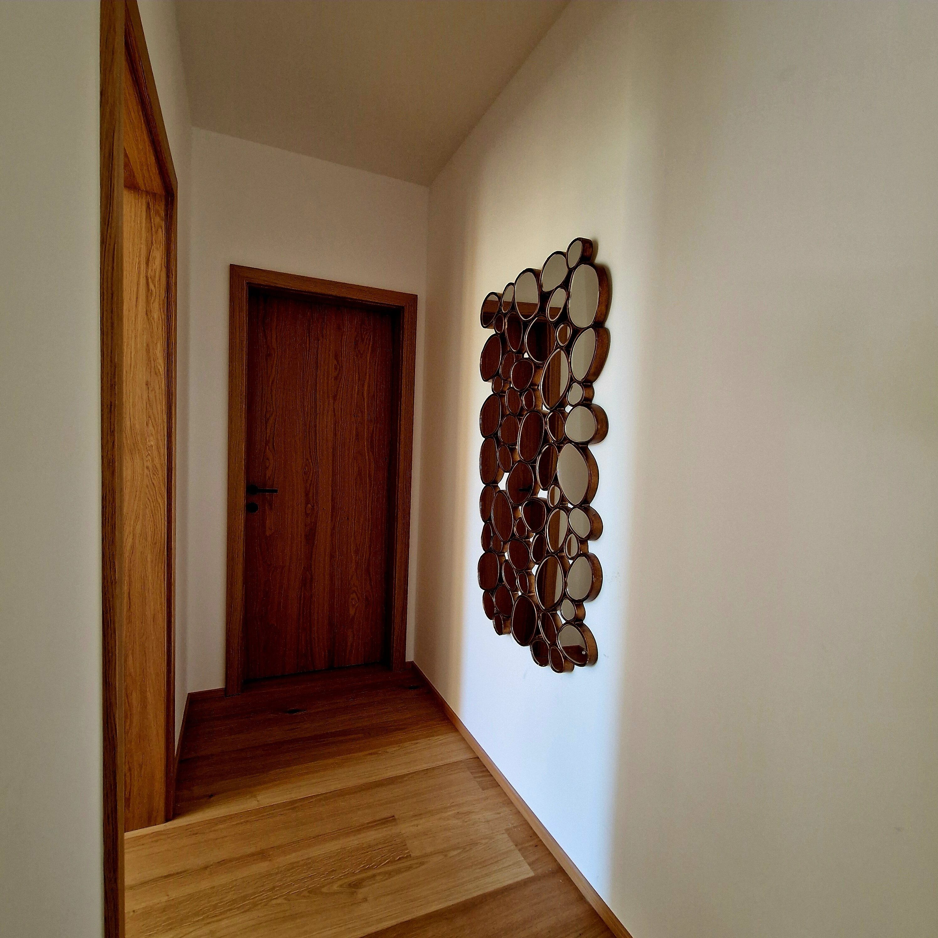 Un pasillo con una puerta de madera y un espejo decorativo en la pared.