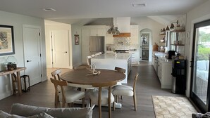 A modern kitchen with white cabinetry, a central island, and a dining area with a round wooden table and chairs. - North Fork Waterfront Oasis in Mattituck (Mattituck)