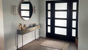 A modern entryway with a dark door, a console table with decorative items, and a large mirror on the wall. - North Fork Waterfront Oasis in Mattituck (Mattituck)
