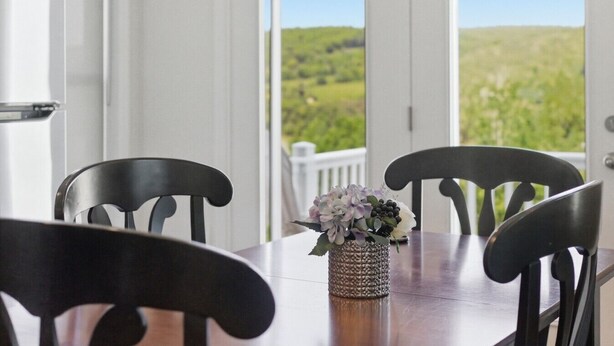 A dining table with chairs, a vase with flowers, and a view of greenery through open doors. - Lakeview Retreat w Fire Pit & Total Privacy! (Lawrenceville)