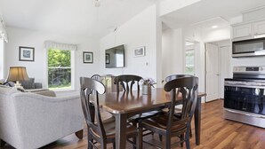 A dining area with a wooden table and chairs, a sofa, a ceiling fan, and a kitchen with an oven. - Lakeview Retreat w Fire Pit & Total Privacy! (Lawrenceville)