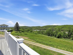A house with a white exterior, a deck, and a view of a green landscape with a road and hills in the distance.