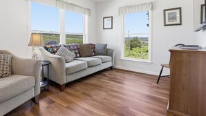 A room with a grey sofa, a wooden desk, and two windows with curtains. - Lakeview Retreat w Fire Pit & Total Privacy! (Lawrenceville)
