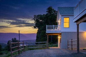 Una casa con balcón, camino de entrada de grava y vista a las montañas.
