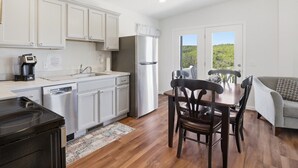A kitchen with white cabinets, a refrigerator, a coffee maker, and a dining area with a table and chairs. - Lakeview Retreat w Fire Pit & Total Privacy! (Lawrenceville)