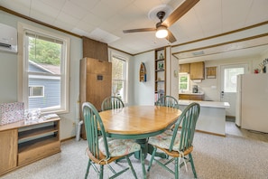 A dining area with a wooden table and green chairs, a ceiling fan, and a kitchen in the background.