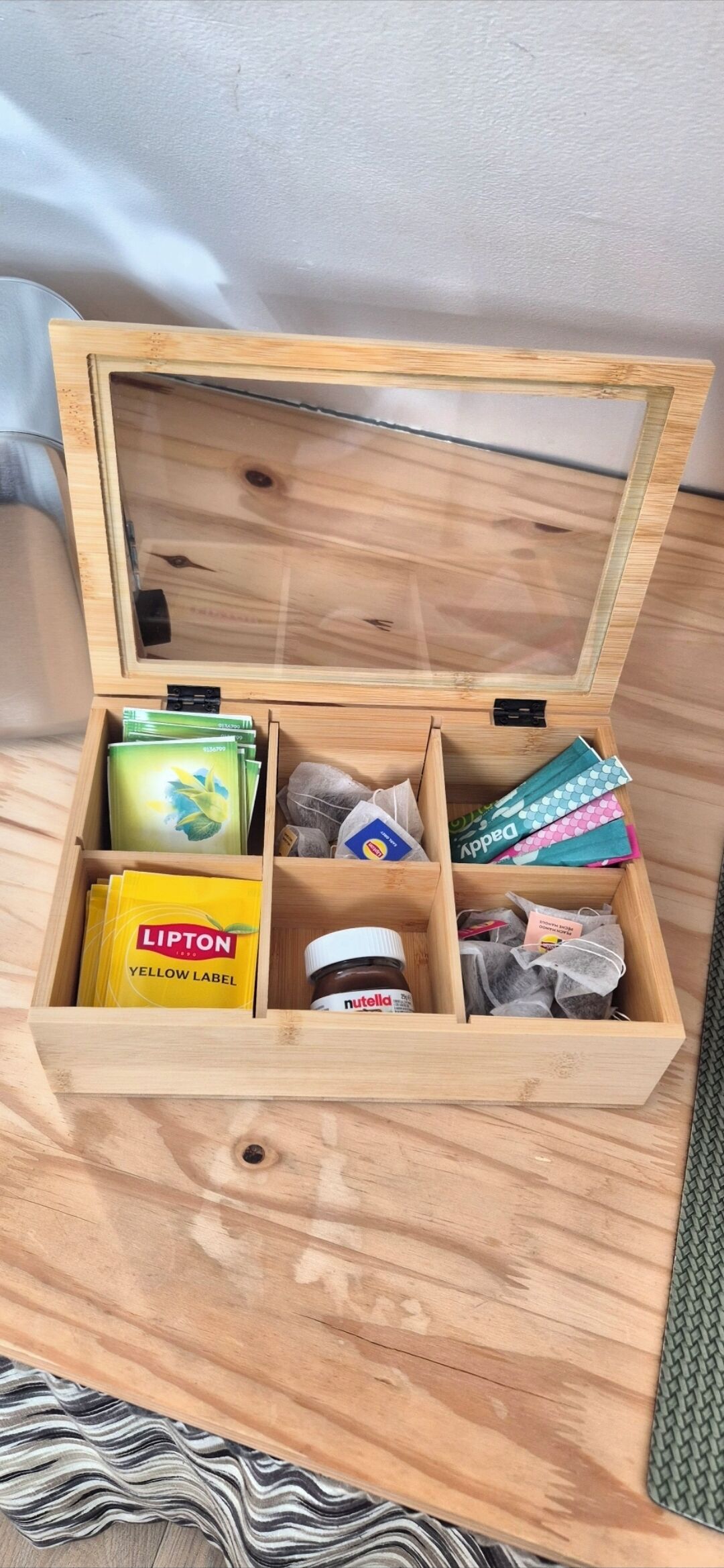 Eine Holzkiste mit Fächern, gefüllt mit verschiedenen Gegenständen wie Lipton Tee, Nutella und anderen Kleinigkeiten.