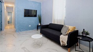 A living room with a dark sofa, a small round table, and a TV mounted on the wall. - Spacious San Juan Home /Parking/ Near Plaza  Las  Americas (San Juan)