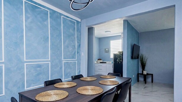 A dining area with a long table, black chairs, woven placemats, and a kitchen in the background. - Spacious San Juan Home /Parking/ Near Plaza  Las  Americas (San Juan)