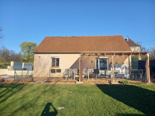 Une maison de plain-pied avec un toit en tuiles, une véranda et une cour clôturée.