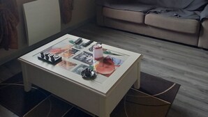 A living room with a white coffee table, a sofa, and a window with curtains.