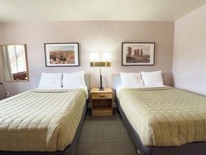 A hotel room with two beds, a nightstand, a lamp, and two framed pictures on the wall.