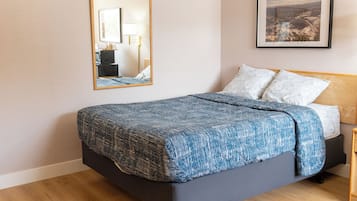 Un dormitorio con cama, espejo, cuadro enmarco y suelo de madera.