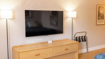 Une chambre d’hôtel équipée d’un téléviseur à écran plat fixé au mur, d’une commode en bois avec des tiroirs, d’un porte-serviettes en métal et d’un tableau encadré accroché au mur.