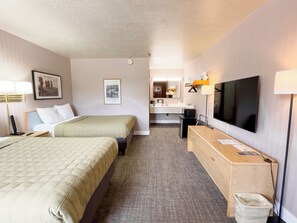 A hotel room with two beds, a desk, a TV, a mirror, and a bathroom visible in the background.