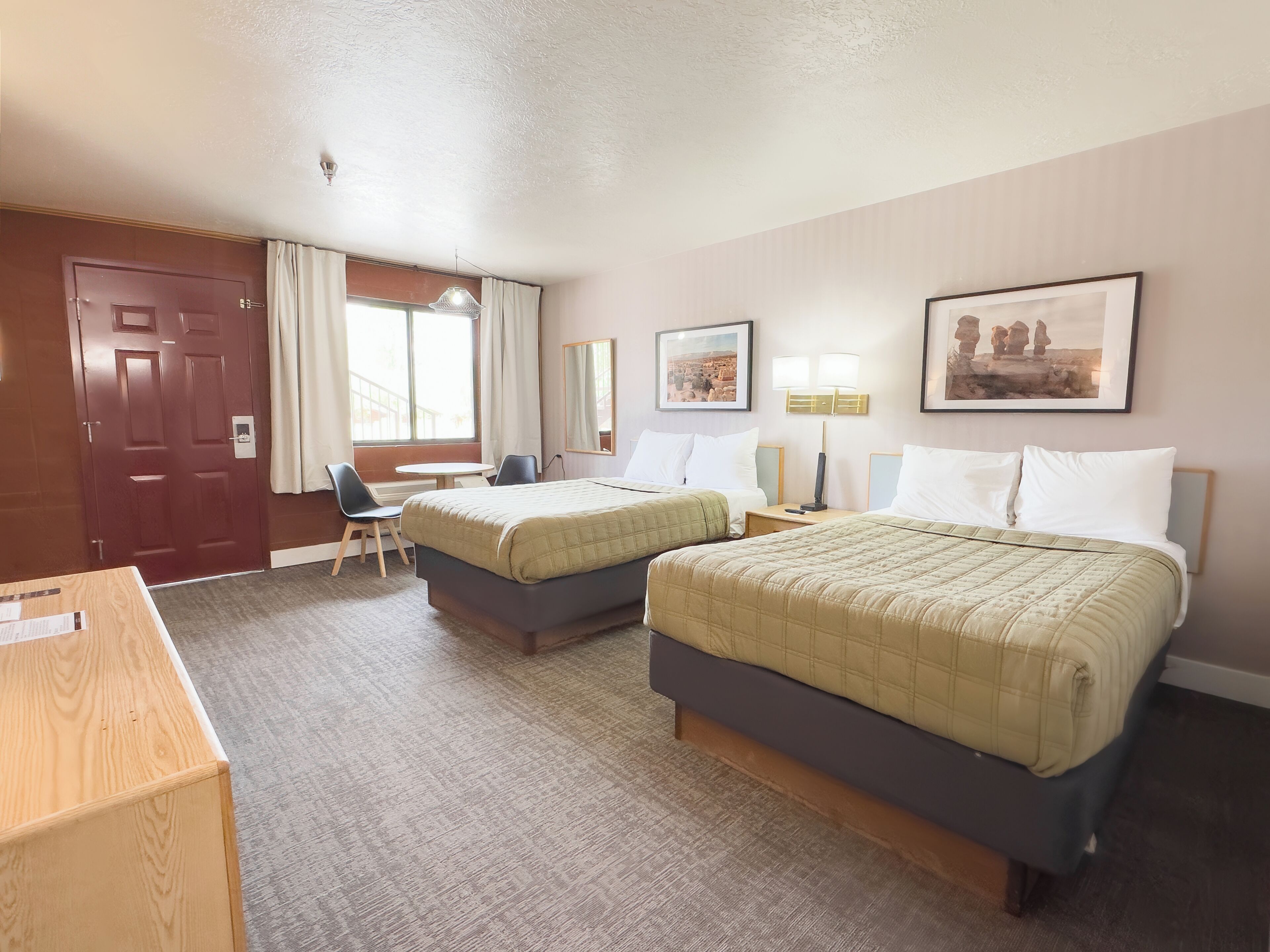 Habitació d'hotel amb dos llits, una taula de treball, una cadira, una finestra amb cortines i una porta.