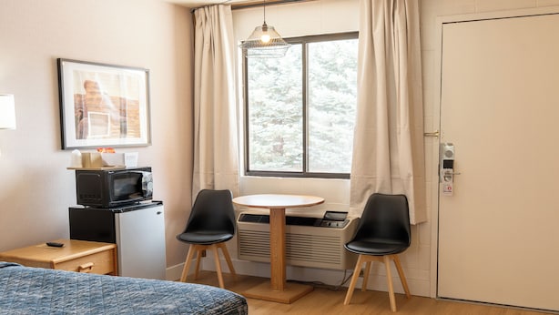 Una habitación con una cama, una mesita pequeña con dos sillas, un microondas, un calentador y una ventana con cortinas.