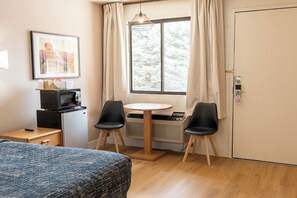 A room with a bed, a small table with two chairs, a microwave, a heater, and a window with curtains. - Prospector Inn (Escalante)