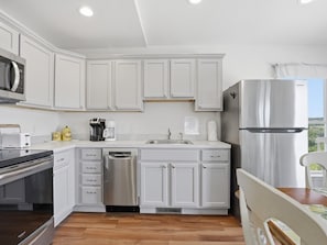 A modern kitchen with white cabinetry, stainless steel appliances, and a wooden floor.