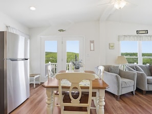 A kitchen with a refrigerator, a dining table with chairs, a sofa, and a view through the windows.