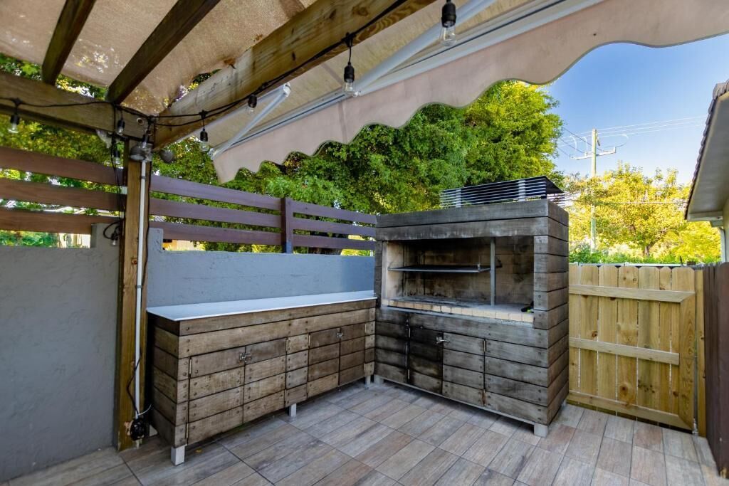 Ett utomhuskök med en inbyggd grill och förvaringsskåp, omgivet av ett trästaket och en pergola med ljusslingor.