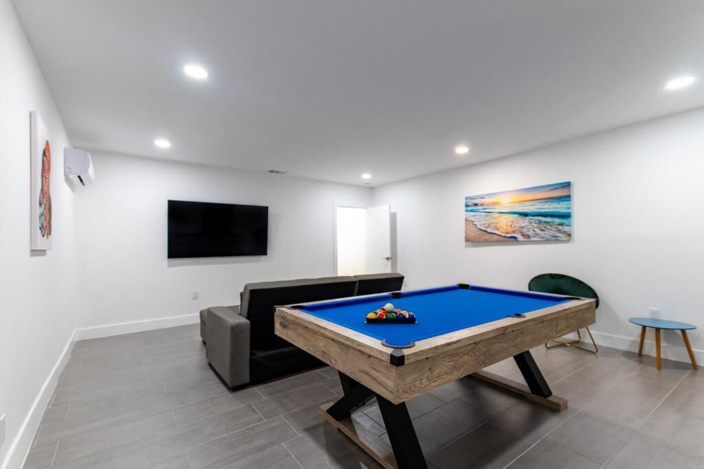 A modern room with a pool table, a flat-screen TV, a sofa, and a painting of a beach scene.