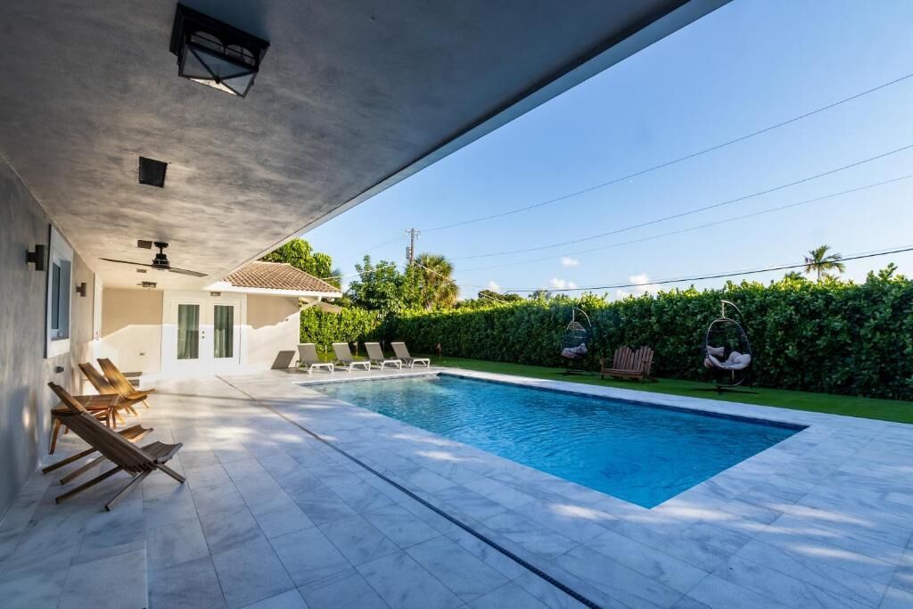 A swimming pool with lounge chairs, a hanging chair, and a small building with a tiled roof.