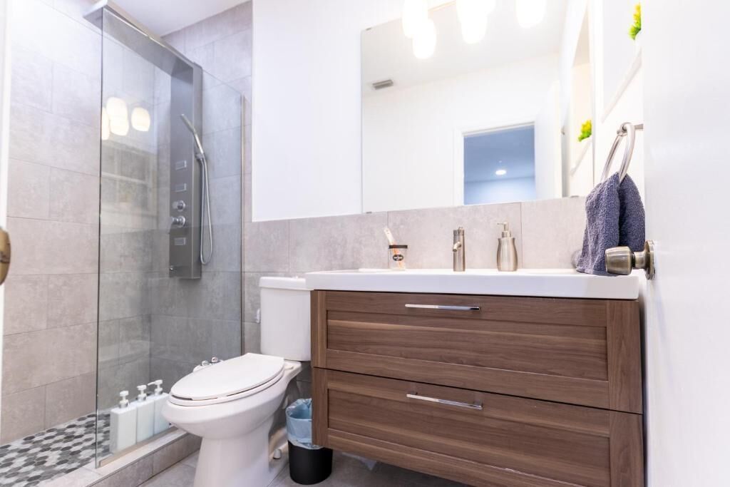 Une salle de bain moderne avec une douche à parois de verre, des toilettes, un meuble-lavabo avec des tiroirs et un miroir.