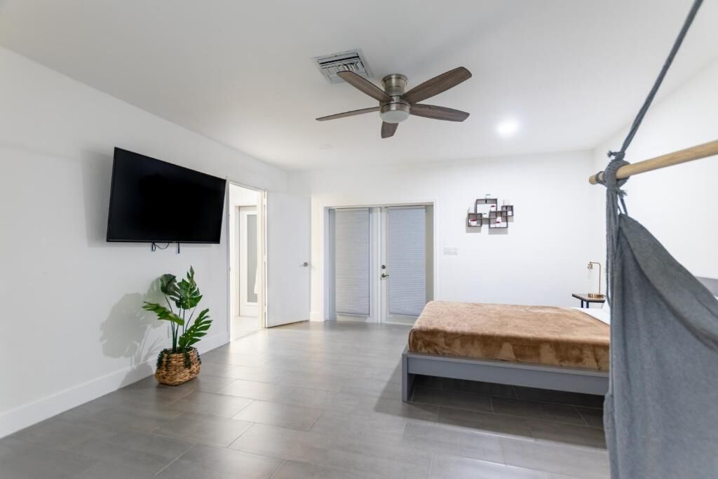 A bedroom with a bed, a ceiling fan, a TV, and a plant.