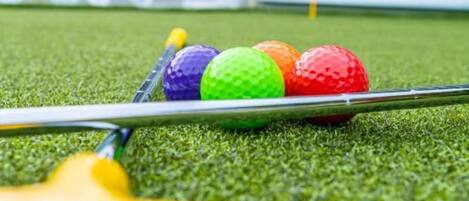 Primer plano de un putting green de golf, con un putter y pelotas de golf al frente.