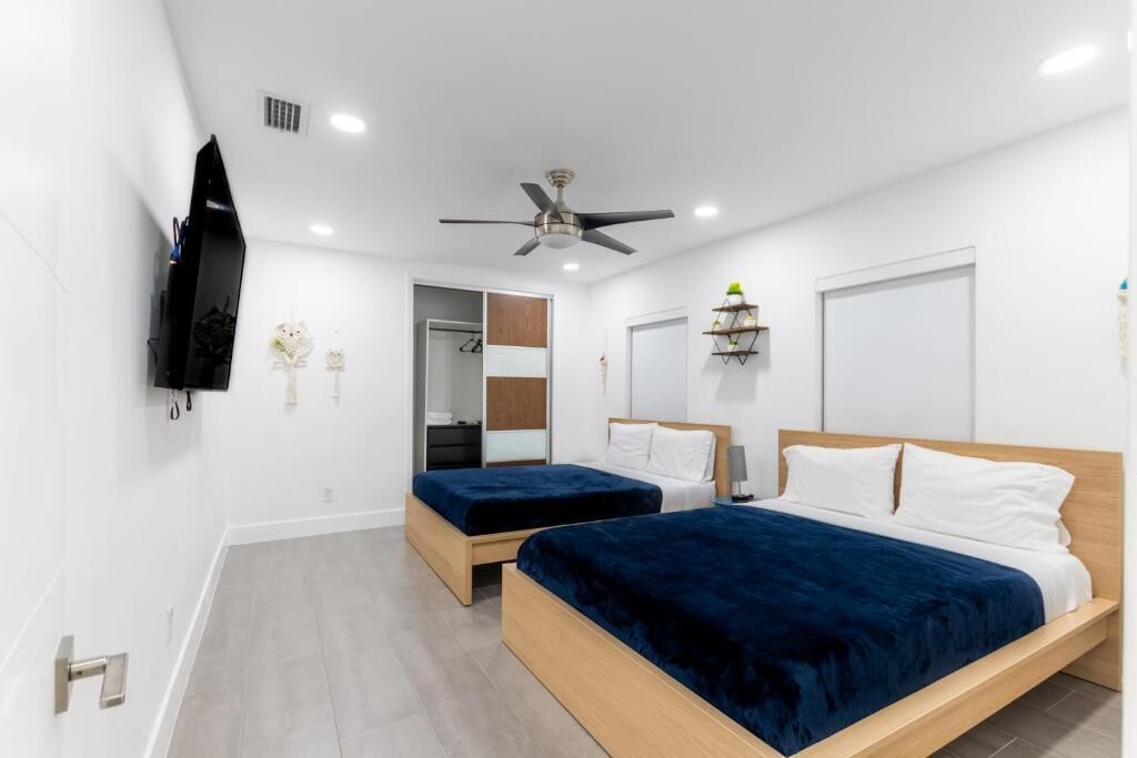 Ein modernes Schlafzimmer mit zwei Betten, einem Deckenventilator, einem Fernseher und einem kleinen Regal mit Dekoration.