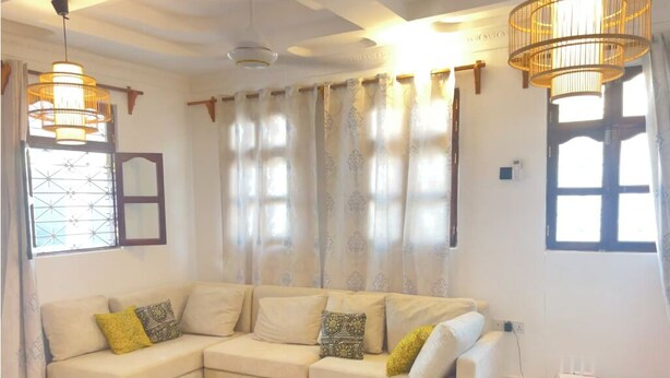 A living room with a beige sectional sofa, patterned cushions, a woven rug, and two pendant lights. - Spacious 4 bedroom Home with Modern Comfort Nungwi (ZANZIBAR)