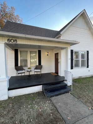 A house with the number 608 on the front, a porch with two chairs, a small table with flowers, and a mailbox. - 2-bedroom house in peaceful Paragould with fenced in backyard (Paragould)