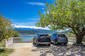 Two cars parked near a tree with a view of a lake and mountains in the background. - Apartment Nikolina 2 with Sea View (Supetarska Draga)