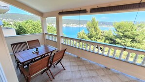 Un balcón con mesa y sillas de madera, suelo de baldosas y vistas a un lago y montañas.