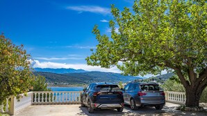 Dos autos estacionados cerca de un árbol con vista a un lago y montañas al fondo.