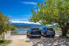 Two cars parked near a tree with a view of a lake and mountains in the background.