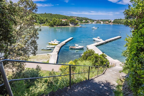 A coastal view with boats docked at a pier, surrounded by greenery and a clear sky.