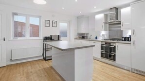 A modern kitchen with white cabinetry, a central island, and built-in appliances. - 3-Bed House with Parking | Ideal for Contractors (Aylesbury)