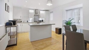 A modern kitchen with white cabinetry, a central island, and a dining area with a table and chairs. - 3-Bed House with Parking | Ideal for Contractors (Aylesbury)
