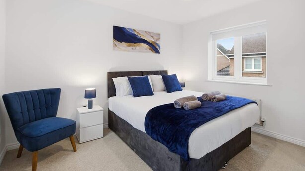 A bedroom with a bed, a chair, a nightstand, a lamp, a window, and a painting on the wall. - 3-Bed House with Parking | Ideal for Contractors (Aylesbury)
