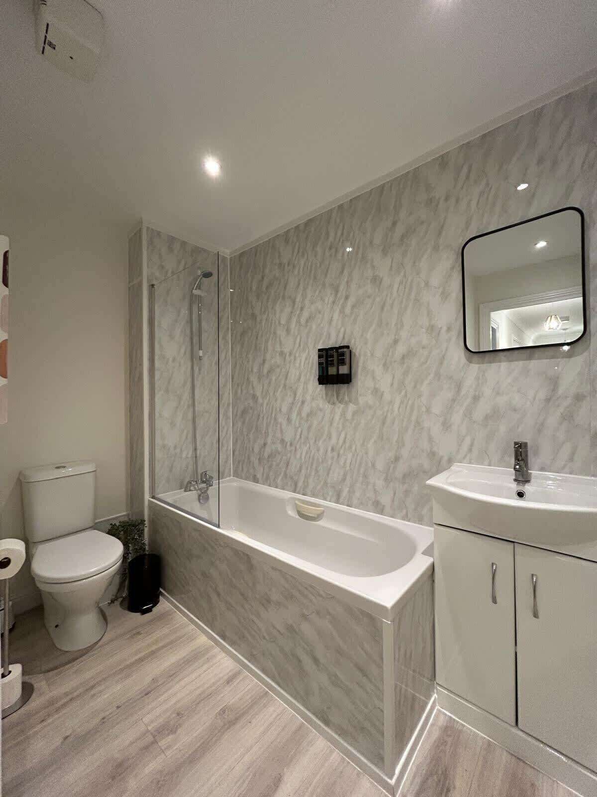 A modern bathroom with a marble wall, a bathtub, a toilet, and a sink.