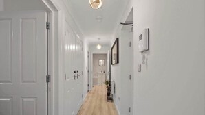 A hallway with white doors, a wooden floor, a hanging light fixture, and a mirror on the wall.