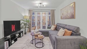 A living room with a sofa, a coffee table, a TV, and a window with curtains.