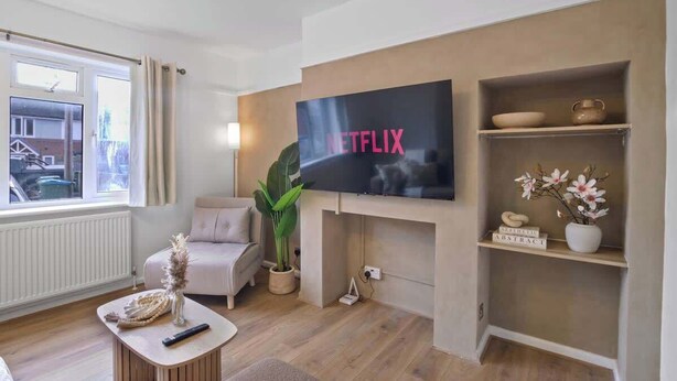 Ein Wohnzimmer mit einem an der Wand befestigten Fernseher, einem Sofa, einem Couchtisch mit einer Vase und einer Pflanze.