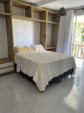 A bedroom with a bed, wooden shelving, a hanging light, and a view through a window. - POUSADA RECANTO TRANCOSO (Porto Seguro)