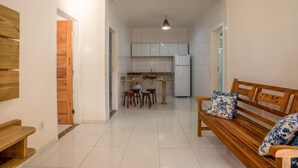 A kitchen with white cabinets, a refrigerator, and a dining area with stools. - POUSADA RECANTO TRANCOSO (Porto Seguro)