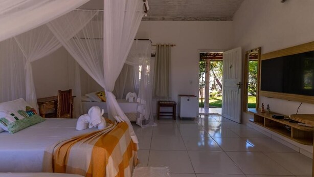 A bedroom with a bed, bedside table, and a TV. - POUSADA RECANTO TRANCOSO (Porto Seguro)